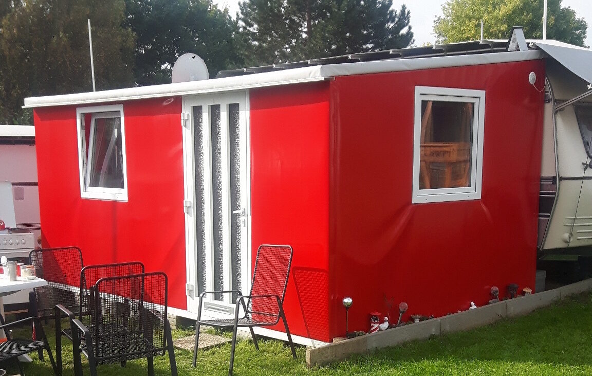 Vorzeltplane in Rot und Weiß auf einem begrünten Campingstellplatz.