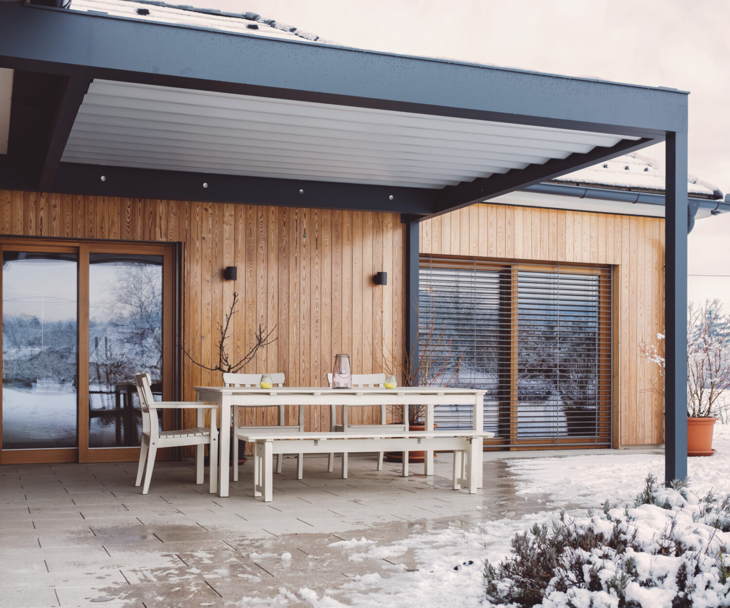 Schneebedeckte Terrasse mit Pergola und weißer Sitzgruppe.