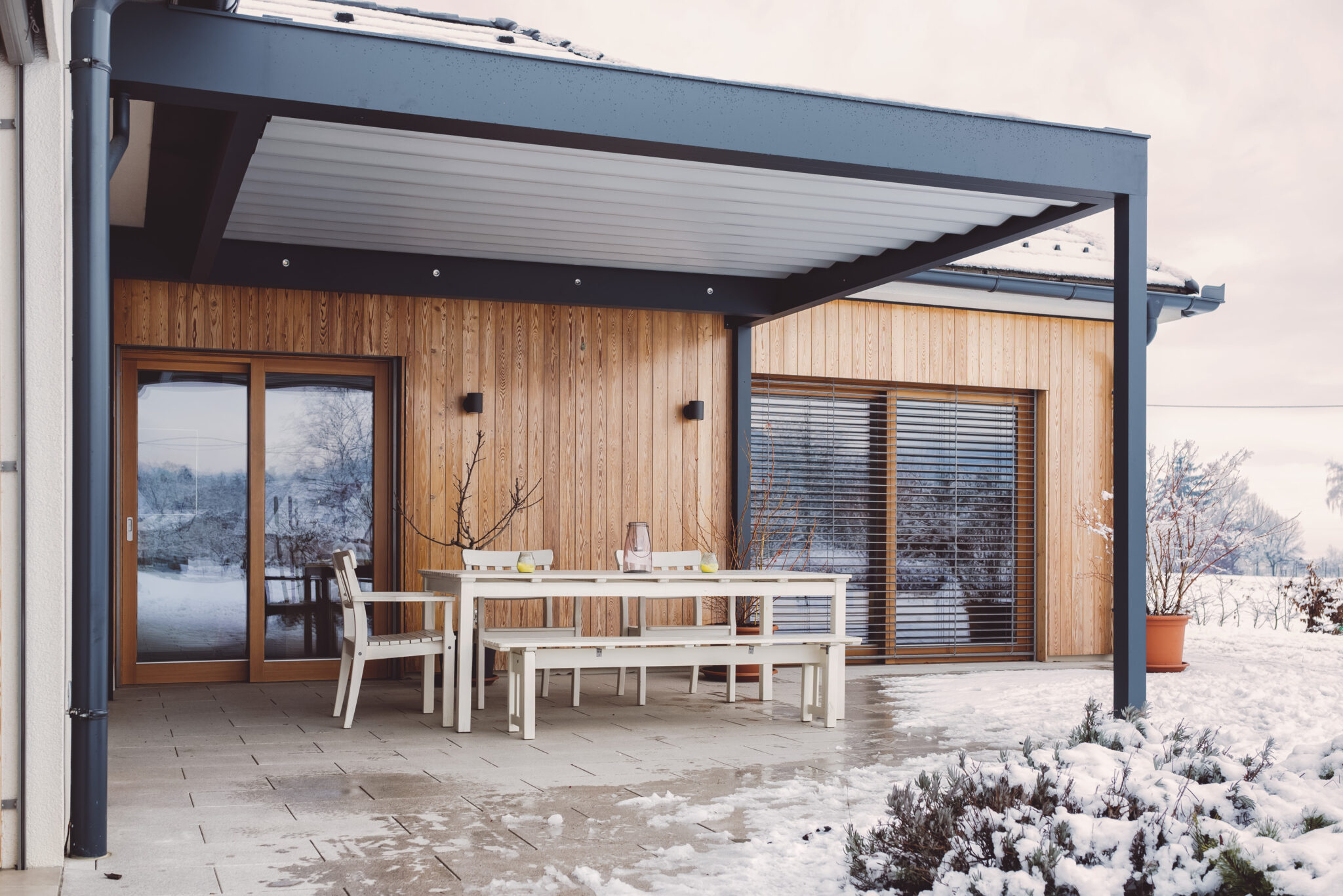 Schneebedeckte Terrasse mit Pergola und weißer Sitzgruppe.